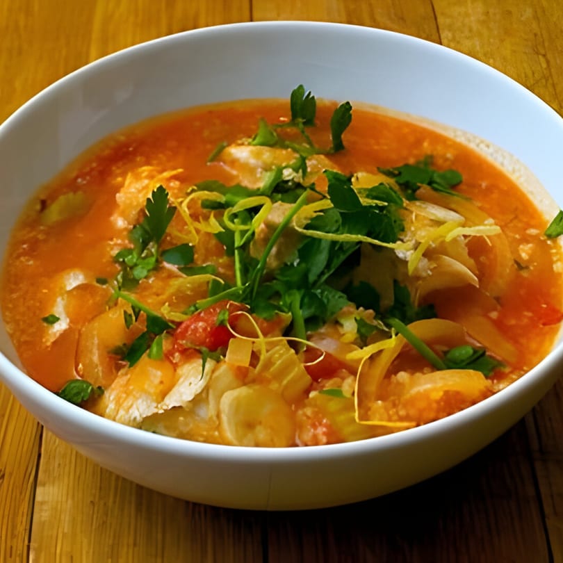 A white bowl of Latin American chicken and vegetable soup, garnished with fresh herbs and lemon zest.