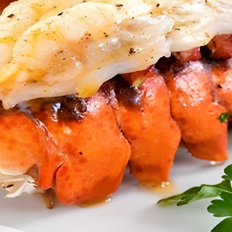 Close-up of grilled lobster tails with melted butter and a sprig of parsley.